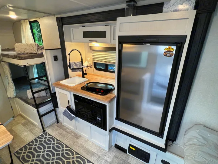 RV rental interior featuring a modern kitchen with a sink, microwave, and stainless steel fridge, plus cozy bunk beds.. No Boundaries 16 2023