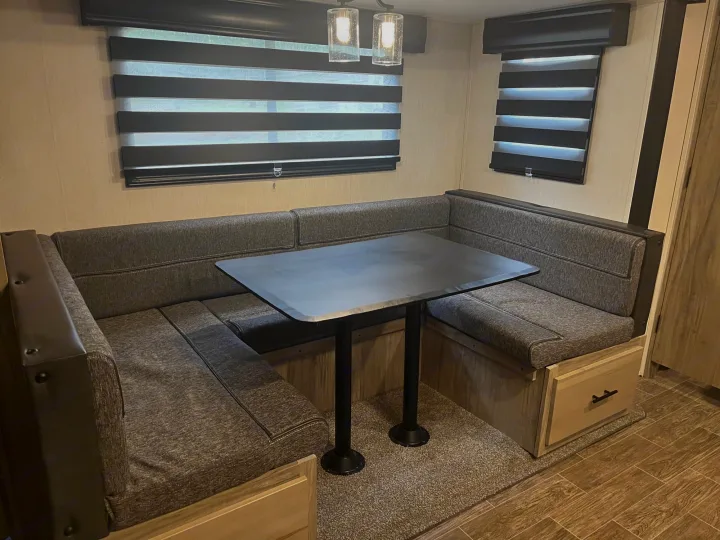 RV rental dinette featuring U-shaped booth seating, a dark table, and striped window blinds, ideal for meals and relaxation.. Forest River Cherokee Alpha Wolf 2022