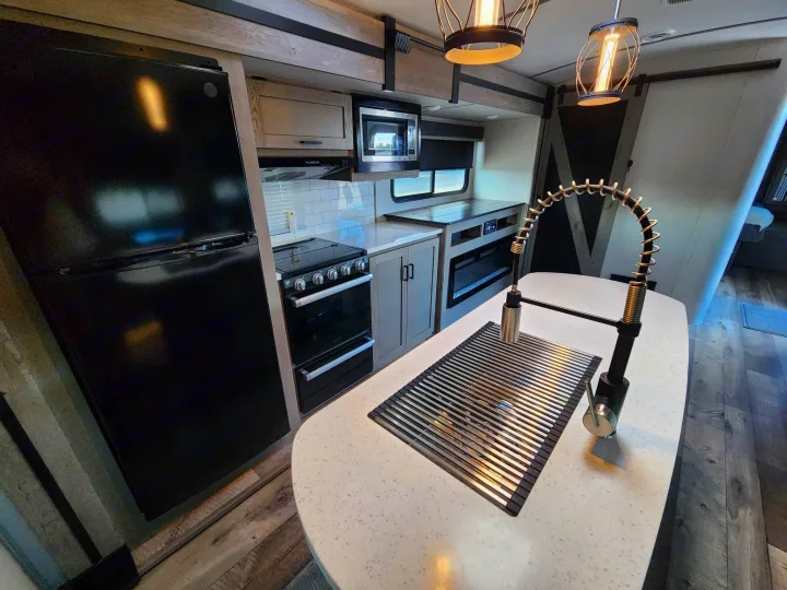 Spacious RV rental kitchen: black appliances, light counters, island sink, and fireplace. Your modern home on wheels.. Keystone Outback 2021