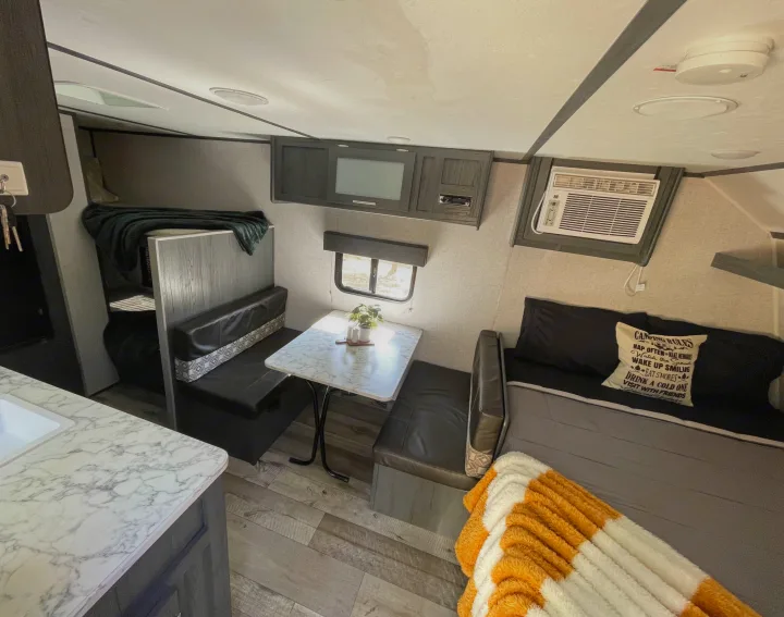 Cozy RV rental interior featuring a dinette, bed, compact kitchen counter, and overhead storage. Ideal for travel adventures.. Dutchmen Aspen Trail 2021