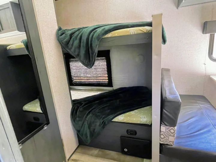 Cozy RV rental interior showing bunk beds with green blankets, a window, and a versatile sleeping/seating area.. Dutchmen Aspen Trail 2021
