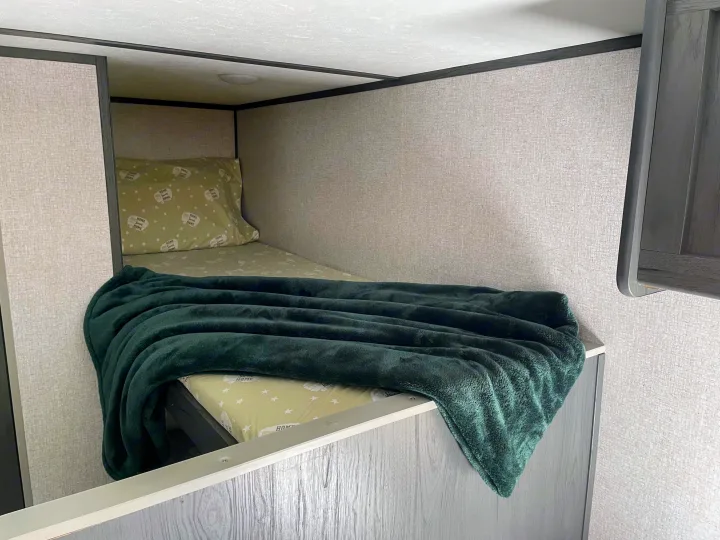 Cozy RV rental bunk bed with "Home Sweet Home" bedding and a soft green blanket, perfect for travel.. Dutchmen Aspen Trail 2021