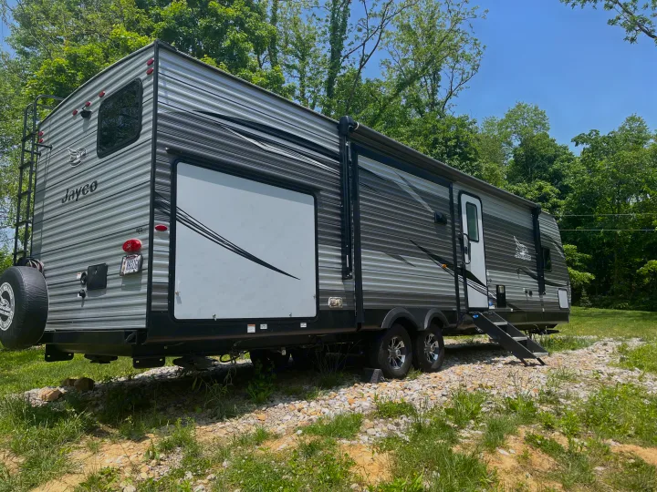 Large grey Jayco travel trailer RV, with an awning & rear ladder, parked in nature. Great for an RV rental trip.. Jayco Jay Flight 2021