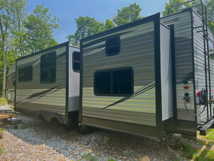 This large RV rental with extended slide-outs is parked on gravel, surrounded by trees. Ideal for outdoor adventures.. Jayco Jay Flight 2021