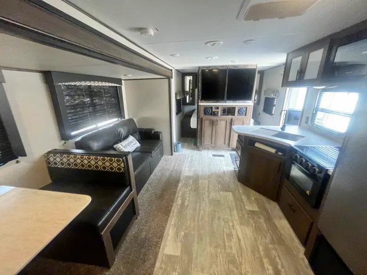 Inside a modern RV rental: a spacious living area, dining booth, full kitchen, and entertainment center are visible.. Avenger Avenger Trailer 2021