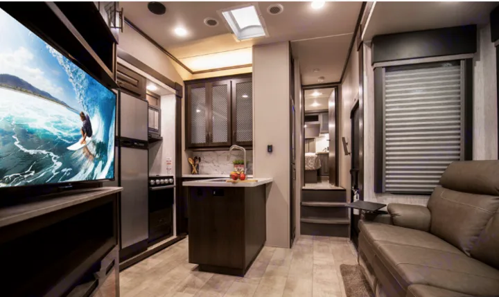 Inside a modern RV rental: a spacious kitchen, living area with a large TV, and comfy sofa.. Grand Design Momentum 2021