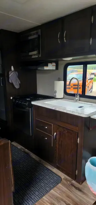 Inside an RV rental: a modern compact kitchen featuring dark cabinets, a stove, microwave, and sink area.. Keystone RV Springdale 2019