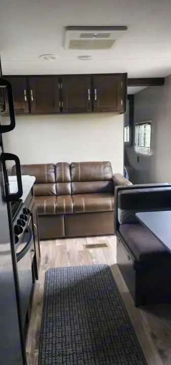 Step inside this cozy RV rental! Features a comfy brown sofa, full kitchen with stove, overhead storage, and dining booth.. Keystone RV Springdale 2019