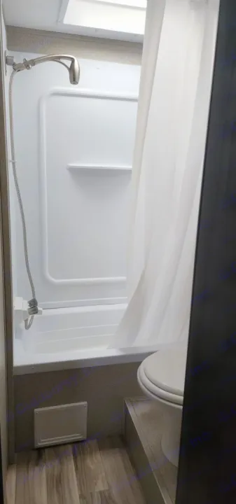 RV rental bathroom interior: white shower/tub, flexible shower head, and skylight. Compact space with wood-look floor.. Keystone RV Springdale 2019