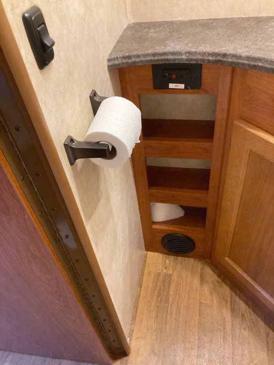 RV rental bathroom: toilet paper holder, GFI outlet on counter, wood storage cabinet, and floor vent.. Coachman Freelander 27QB 2011