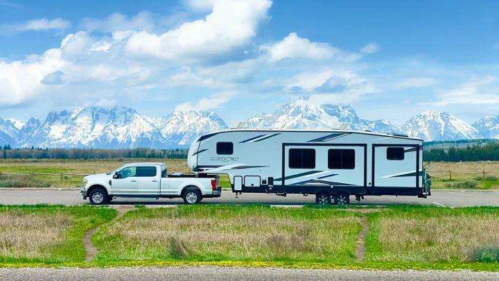 An RV rental (white truck + fifth-wheel) parked with Grand Teton's snowy peaks in the background, a perfect outdoor adventure.. Forest River Cherokee Arctic Wolf 2022