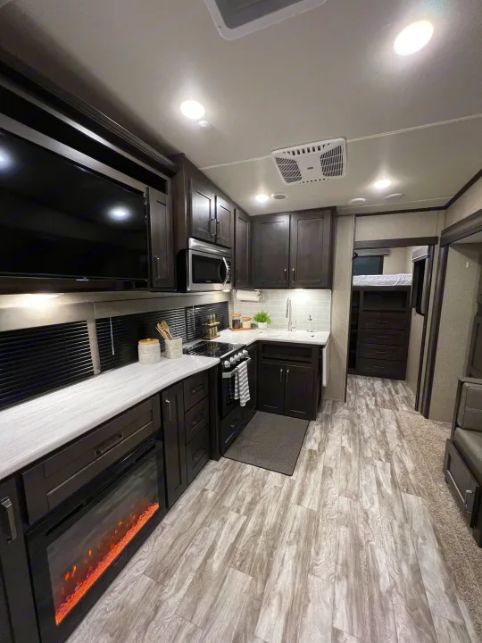 Spacious RV rental interior: modern kitchen with dark cabinets, light counters, and a fireplace. Also a TV & bunks.. Grand Design Reflection 2021