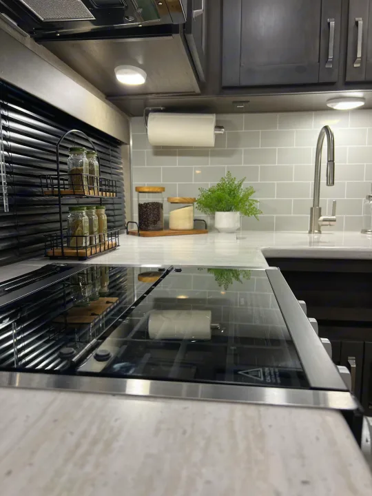 Modern RV rental kitchen showcasing a sleek induction cooktop, organized spices, and bright under-cabinet lighting.. Grand Design Reflection 2021