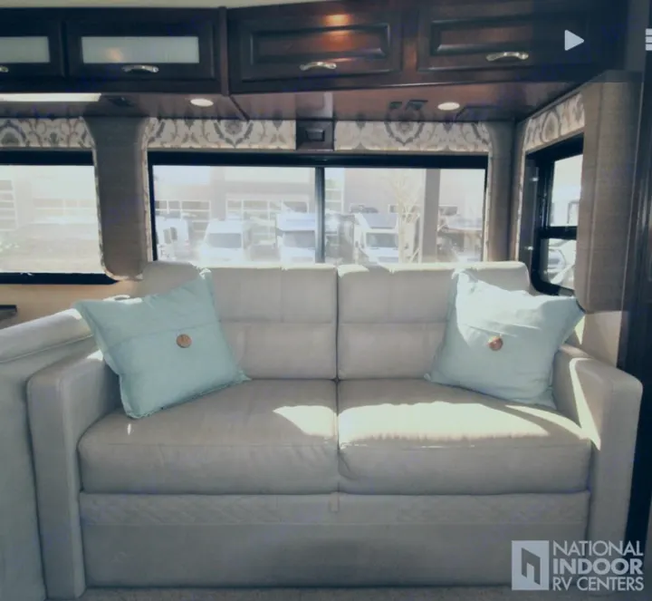 Cozy RV living space: a light sofa with pillows, wood cabinets, and scenic windows. Explore your next RV rental.. Fleetwood Bounder 2017