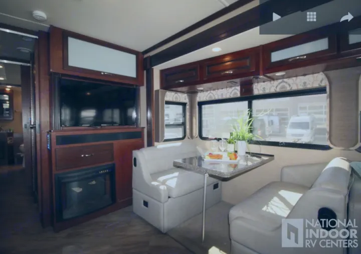 Modern RV rental interior featuring a comfortable dinette with table settings, TV, and fireplace for travel comfort.. Fleetwood Bounder 2017