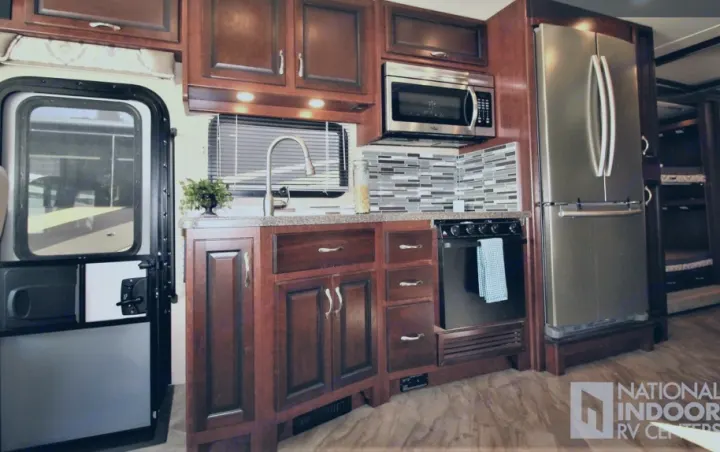 Spacious RV rental kitchen with dark wood cabinetry and modern appliances: microwave, stove, fridge. Ideal for travel.. Fleetwood Bounder 2017