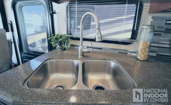Inside an RV rental, a clean kitchen features a double stainless steel sink, modern faucet, and speckled countertop.. Fleetwood Bounder 2017