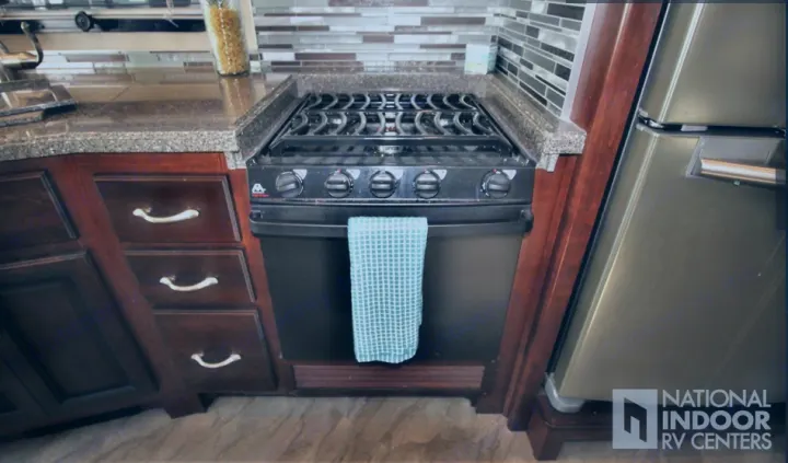 RV rental's compact kitchen: 4-burner stovetop, oven, dark wood cabinets, and granite-look counters. Essential for mobile cooking.. Fleetwood Bounder 2017