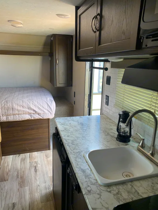 Cozy RV rental interior with a bright kitchen, sink, and a comfortable bed. Ideal for your next road trip adventure!. Keystone RV Springdale 2018