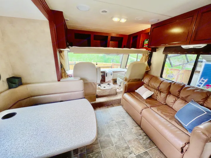 An RV rental's inviting interior: a dining booth, comfy brown sofa, and front cockpit with overhead bed.. A.C.E. A.C.E. Motorhome 2013