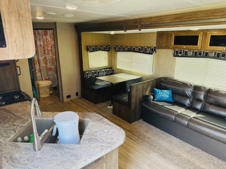 RV rental interior: well-appointed living space with kitchenette, dining booth, sofa, and visible bathroom in the background.. Dutchmen Coleman Lantern 2019