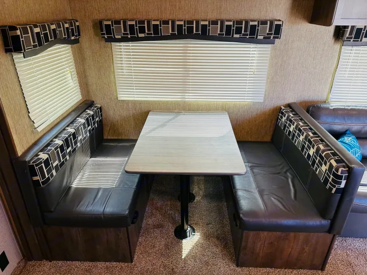 RV rental dinette: Dark faux leather benches, patterned backrests, and a table. Sunlight streams through blinds.. Dutchmen Coleman Lantern 2019