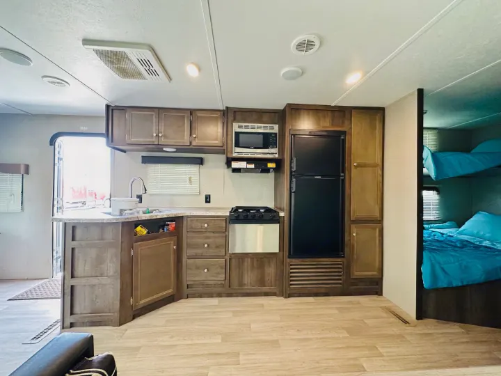 Modern RV rental interior showcasing a well-equipped kitchen with fridge, stove, microwave, plus comfortable bunk beds.. Dutchmen Coleman Lantern 2019