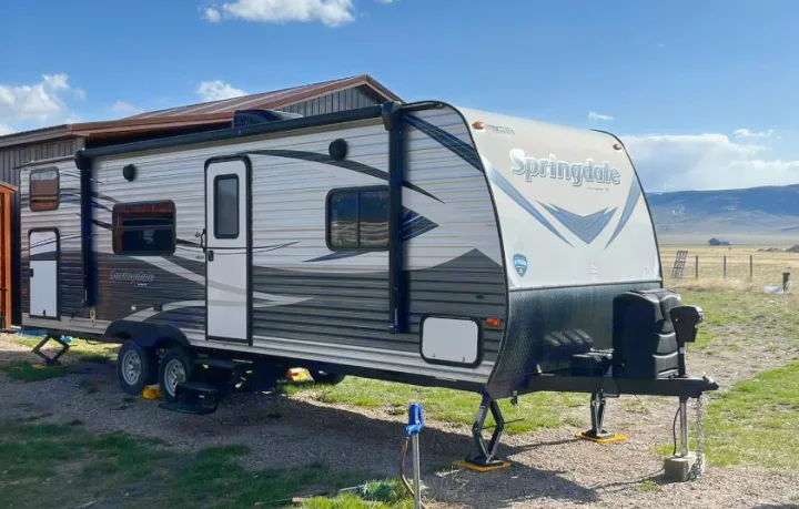 This Springdale travel trailer makes a great rv rental, parked outdoors with a barn & mountains in the background.. Keystone RV Springdale 2019