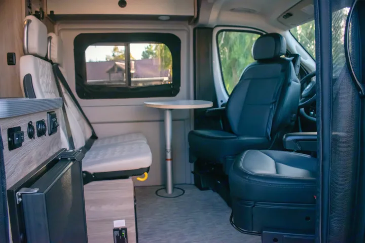 RV rental interior showing versatile seating, a dinette table, and compact fridge, ready for your road trip adventures.. Winnebago Solis 59PX 2023