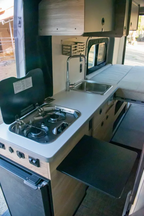 RV rental: compact camper van interior with kitchenette (stove, sink, fridge), pull-out table, and bed. Ready for adventure!. Winnebago Solis 59PX 2023