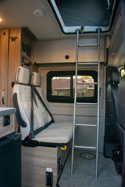 Inside an **RV rental**: a bright **camper van** interior with a ladder to an **overhead bunk**, comfortable seating, and wood accents.. Winnebago Solis 59PX 2023