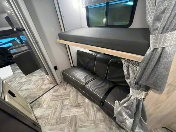 Cozy RV rental interior with a bunk bed over a black sofa, complete with seatbelts, patterned curtains, and wood-look floor.. Forester LE 2022