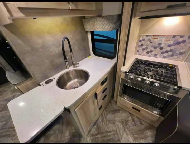 Modern RV rental kitchen with a stainless steel sink, gas range, oven, and extendable countertop for convenience.. Forester LE 2022