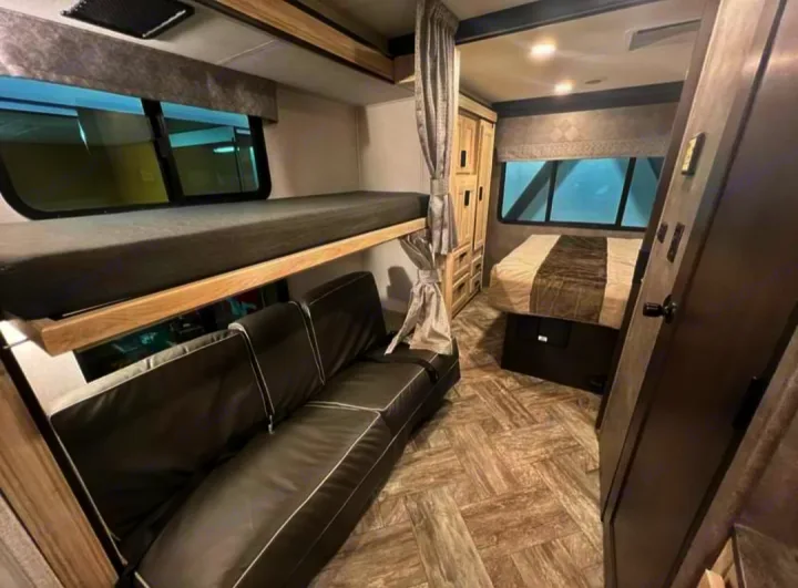 Modern RV rental interior featuring bunk beds above a sofa, a separate main bed, and ample storage cabinetry. Ready for your travels.. Forester LE 2022