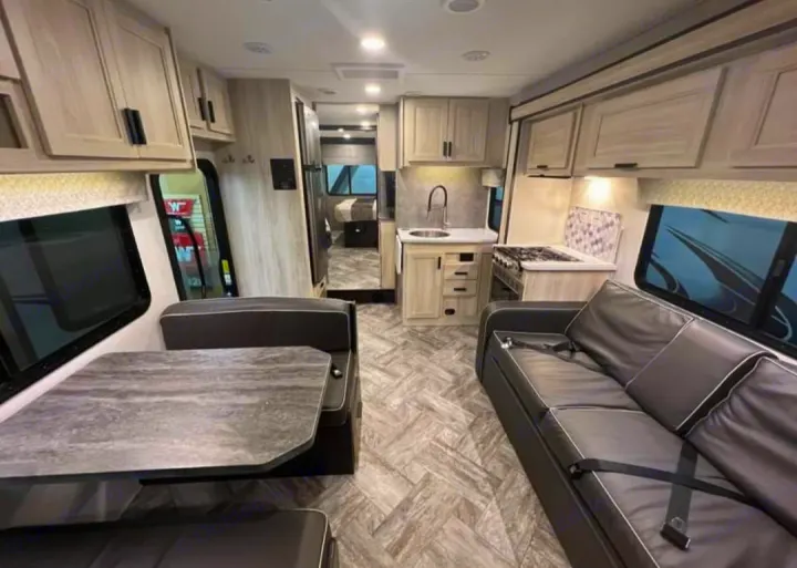 Bright & modern **rv rental** interior with kitchen, dinette, & sofa. Light wood cabinets, dark seating. Spacious for travel.. Forester LE 2022