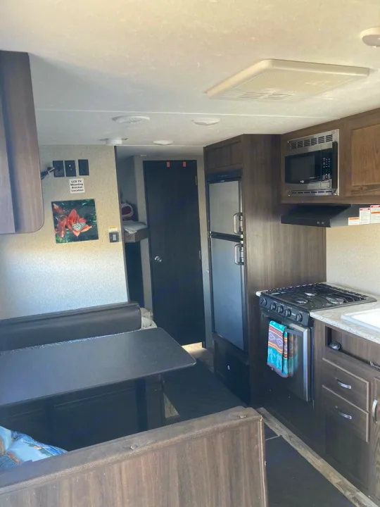 View of an RV rental's interior, showing a dinette with table and a full kitchen area with stove, microwave, and fridge.. Keystone RV Springdale 2019