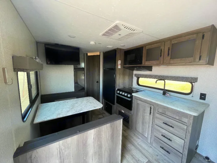 Inside this RV rental: a modern kitchen with stove, microwave, sink, and fridge, plus a dining area and TV.. KZ Sportsmen SE 260BHSE 2022