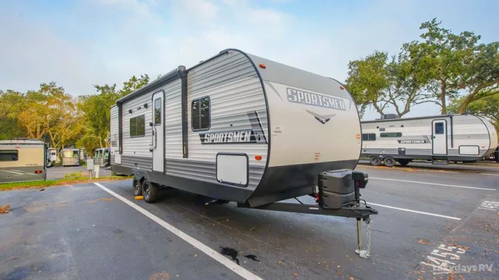 A modern Sportsmen travel trailer, ideal for an RV rental, is parked in a large lot with other recreational vehicles.. KZ Sportsmen SE 260BHSE 2022