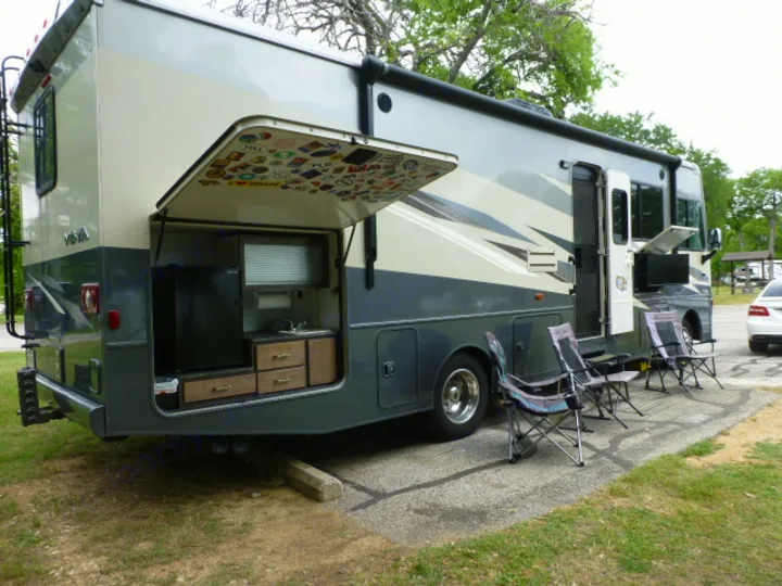 This rv rental offers an exterior kitchen (sticker-covered hatch), outdoor TV, and chairs, perfect for camping.. Winnebago Vista 2020