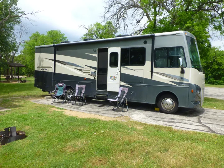 Winnebago Vista RV rental set up at a green campsite with chairs and a fire pit for outdoor adventures.. Winnebago Vista 2020