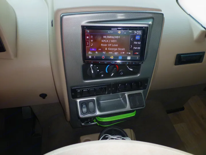 An RV rental's central dash shows a Kenwood stereo playing 99.5 KPLX, with climate controls below.. Winnebago Vista 2020