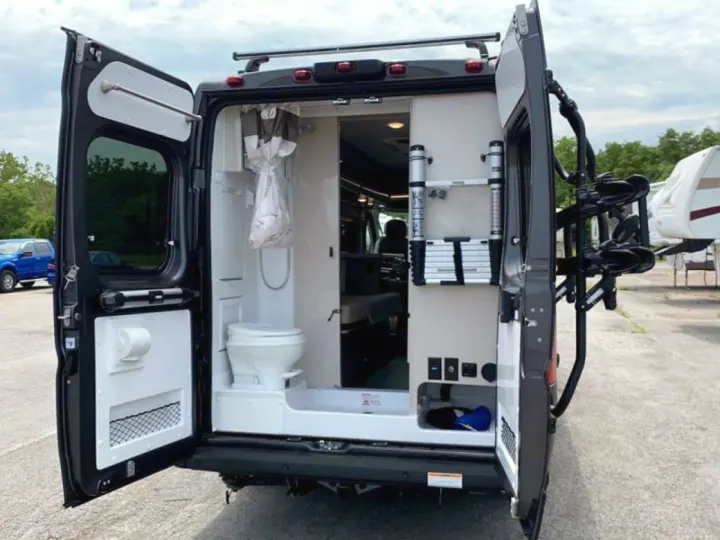 This **rv rental** camper van, viewed from the rear with open doors, showcases its compact bathroom with toilet/shower, interior, and bike rack.. Thor Sequence 2020