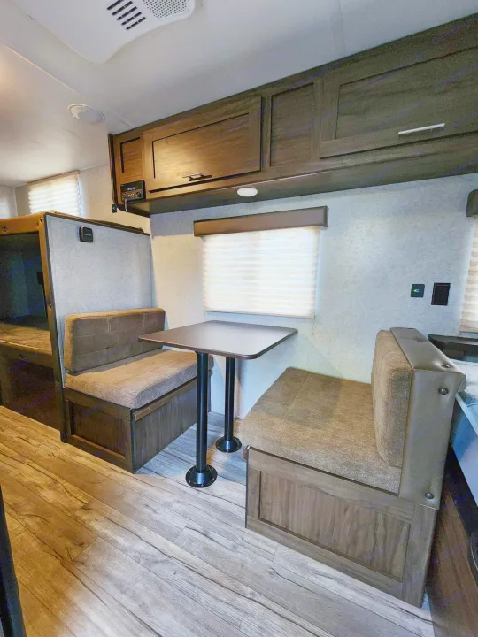 Inside an RV rental: a modern dinette with comfy benches, bunk beds, and dark wood cabinets for storage.. Forest River Cherokee Wolf Pup 2018