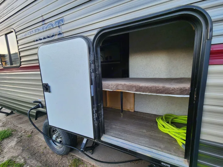 Open side access door of an RV rental, revealing a bunk bed, wood floor, and a coiled green hose inside.. Forest River Cherokee Wolf Pup 2018