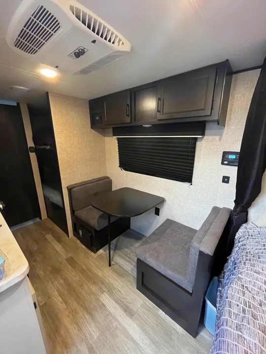 RV rental interior: A practical living area with dinette, overhead cabinets, bunk beds on the left, AC, and wood-look floor.. Jayco Jay Flight SLX 2023