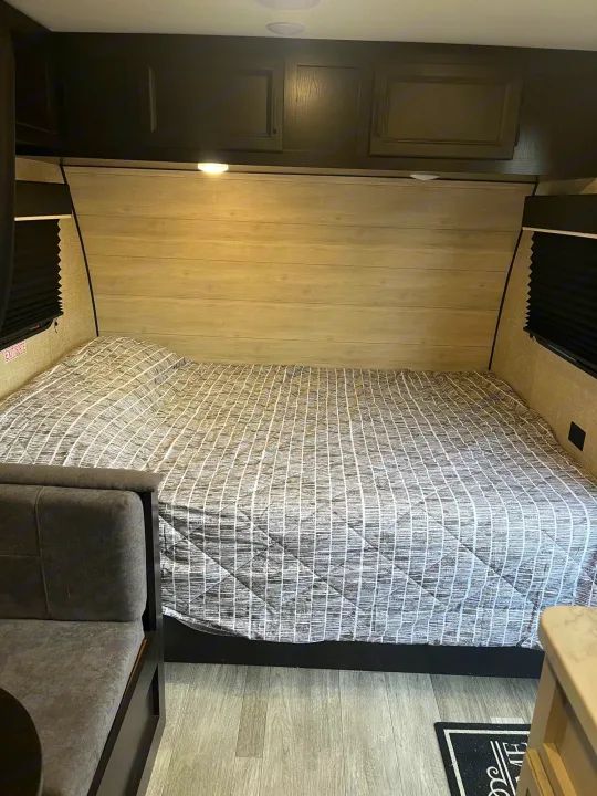 Cozy RV rental bedroom featuring a large bed with a gray comforter, overhead storage, and dinette seating.. Jayco Jay Flight SLX 2023