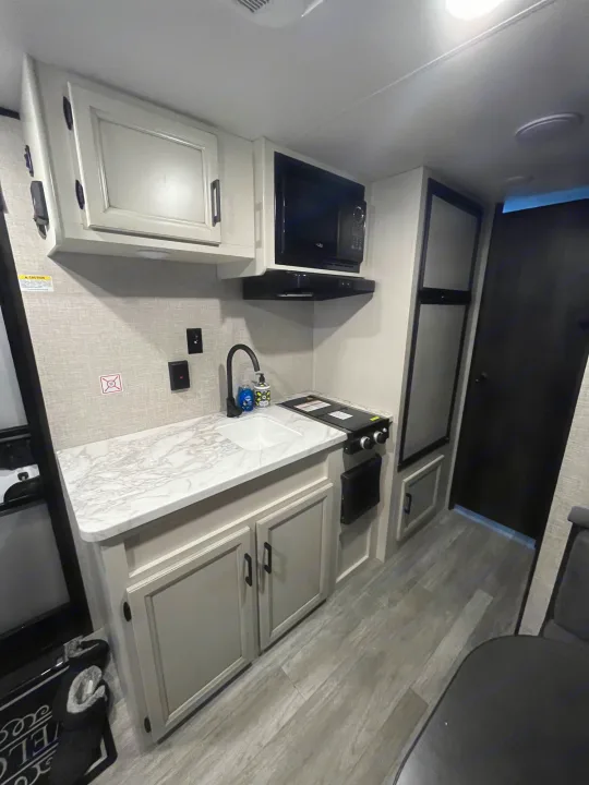 Modern RV rental galley: neutral cabinets, marble counter, sink, cooktop, microwave, and fridge. Compact & well-equipped.. Jayco Jay Flight SLX 2023