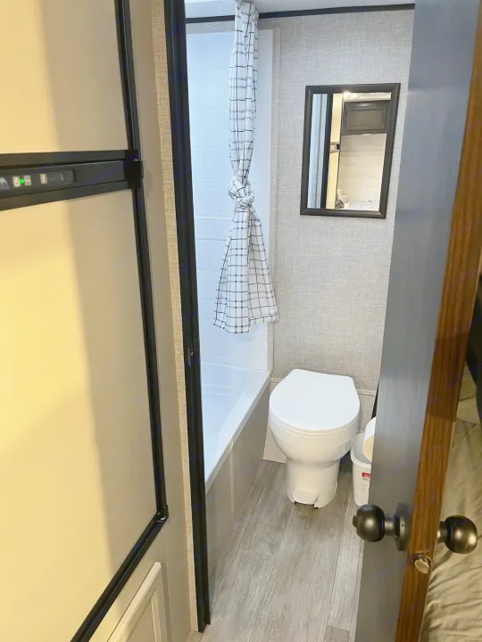 Compact RV rental bathroom features a toilet, tub/shower, mirror, and nearby refrigerator section.. Jayco Jay Flight SLX 2023