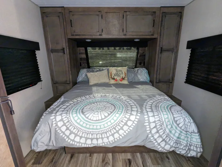 Cozy RV rental bedroom with a gray patterned comforter on the bed, flanked by dark wood cabinets and blackout blinds.. Sport Trek Sport Trek Trailer 2021
