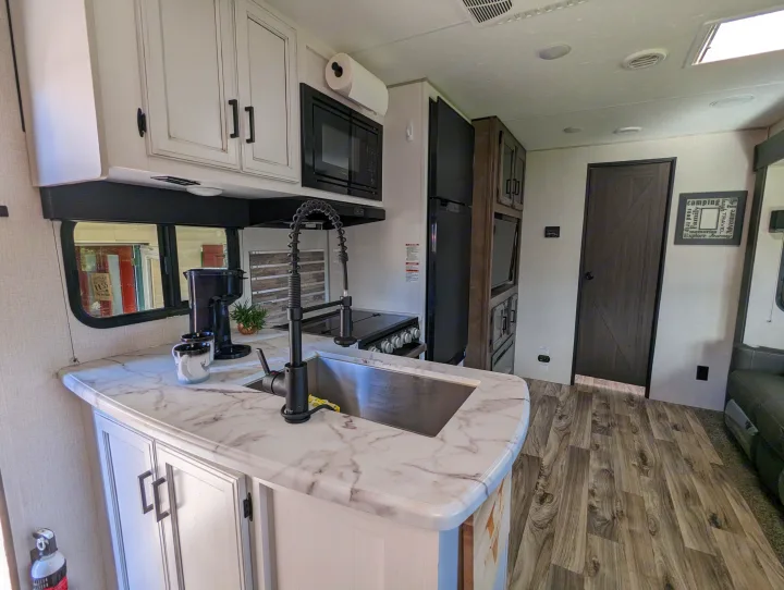 Modern RV rental kitchen with white cabinets, marble-look counters, and appliances, ready for your road trip.. Sport Trek Sport Trek Trailer 2021